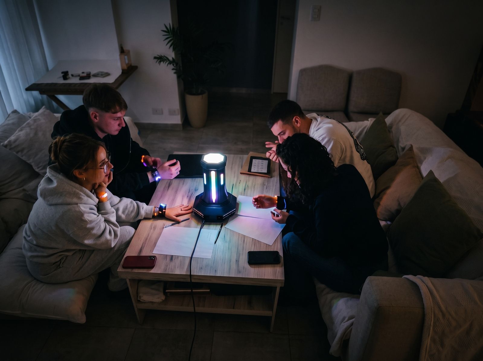 Un grupo alrededor de una mesa, con pulseras en la muñeca, resolviendo un desafío junto al tótem encendido